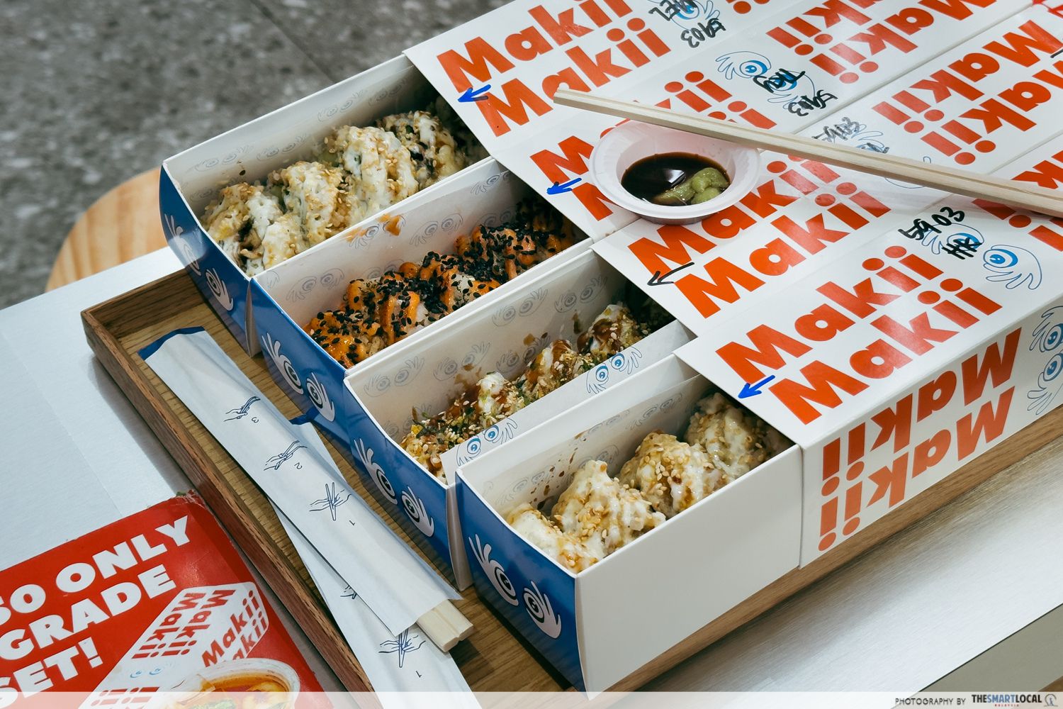 four maki rolls served in rectangular drawer boxes, paired with wasabi and soya sauce