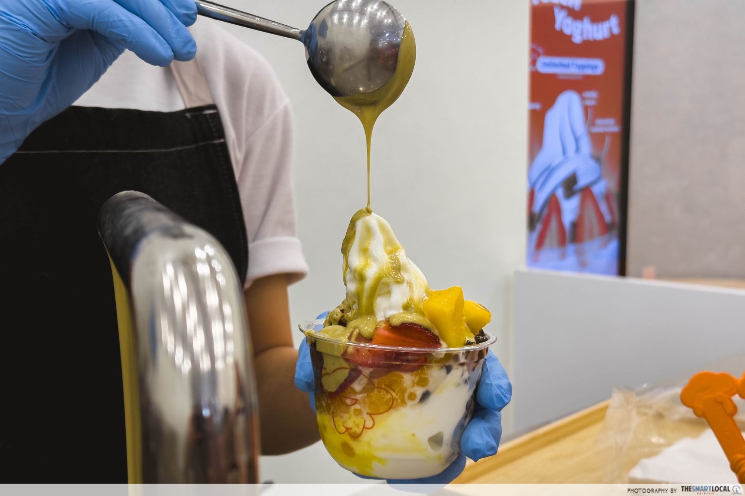 pistachio sauce is drizzled onto a cup of froyo stuffed with toppings such as fruits, popping pearls, etc.