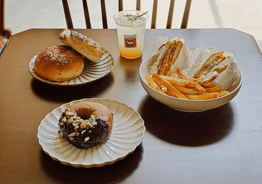 two pieces of plain sesame bagels, a bagel sandwich with fries, and a bagel half-coated with chocolate sauce on the table