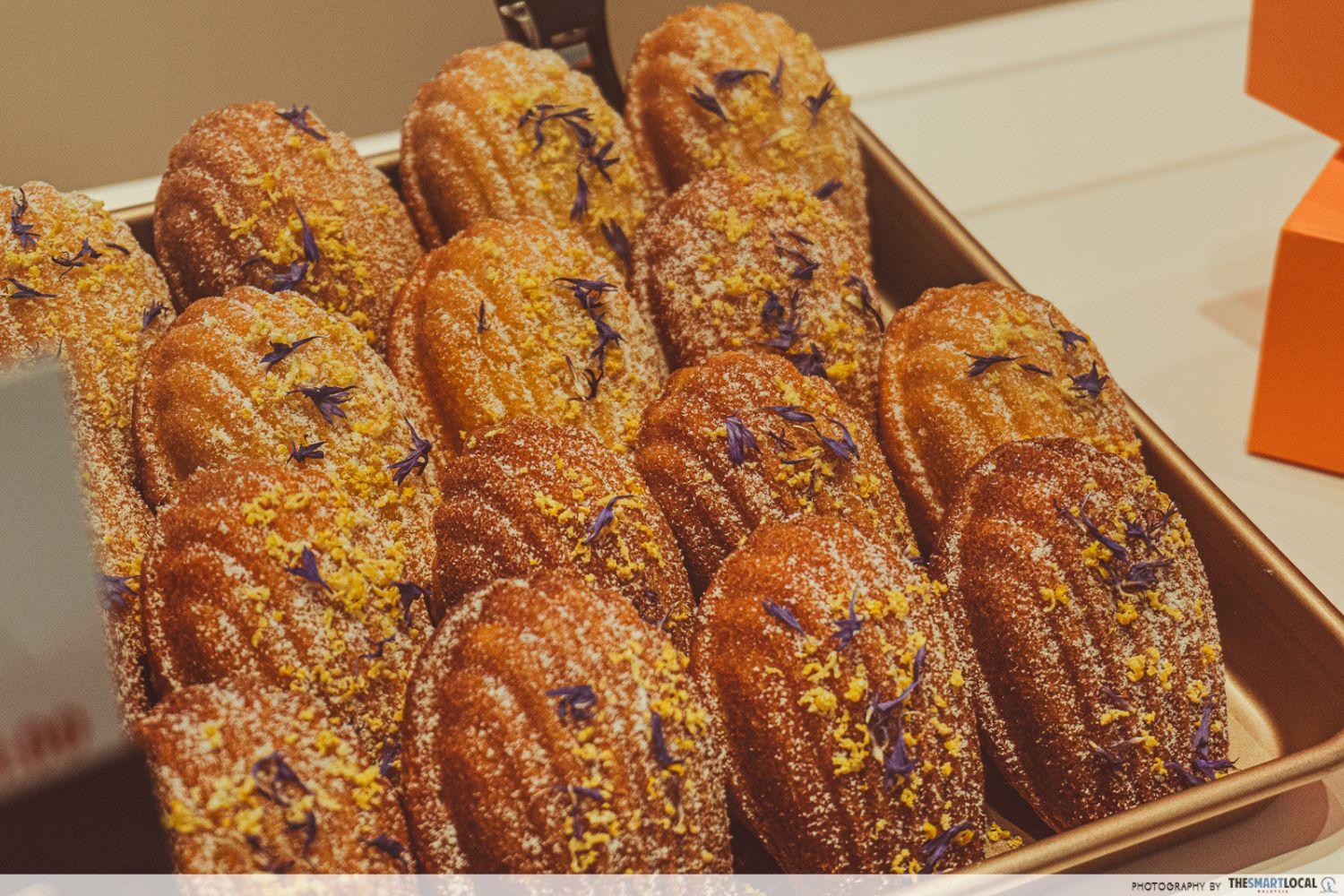 a tray of lemon madeleines sprinkled with powdered sugar and lemon zest